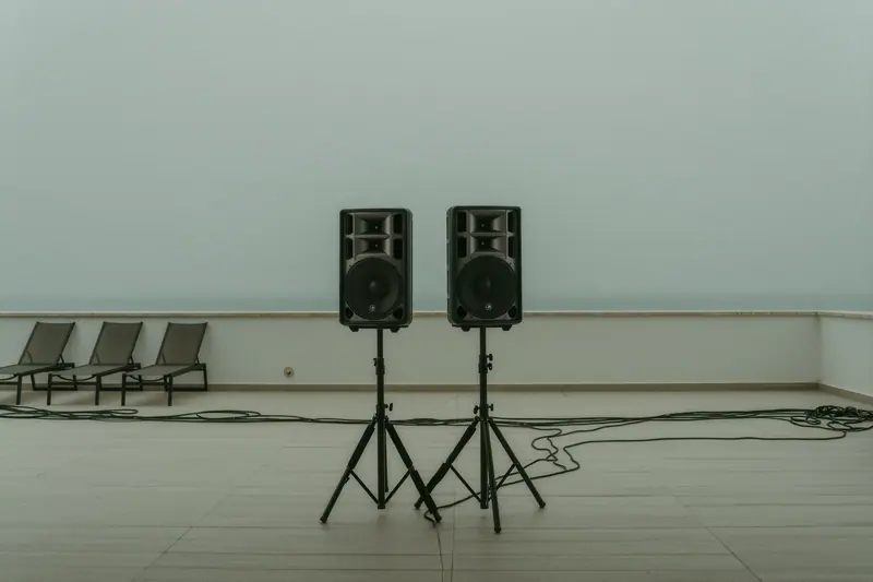 A pair of PA speakers on stands facing an empty villa terrace at dusk, cables taped down along the paving.