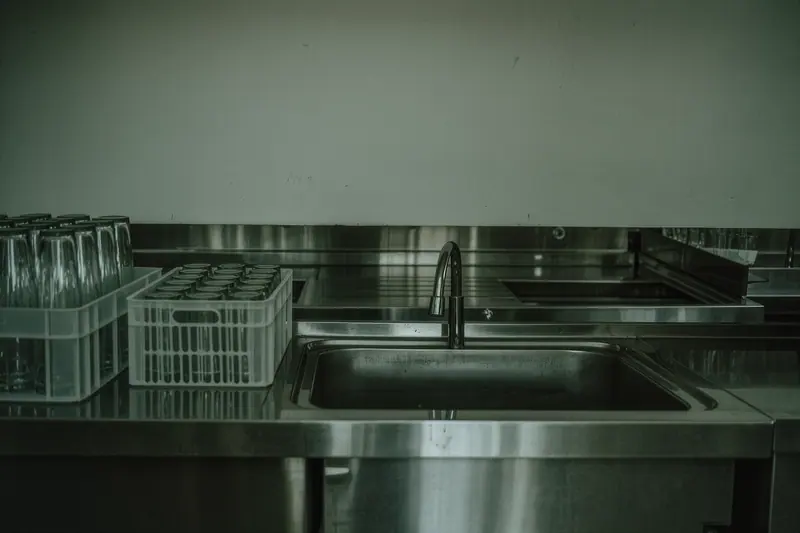 A bare service kitchen with stainless steel counters and stacked glassware, no appliances plugged in, no people.