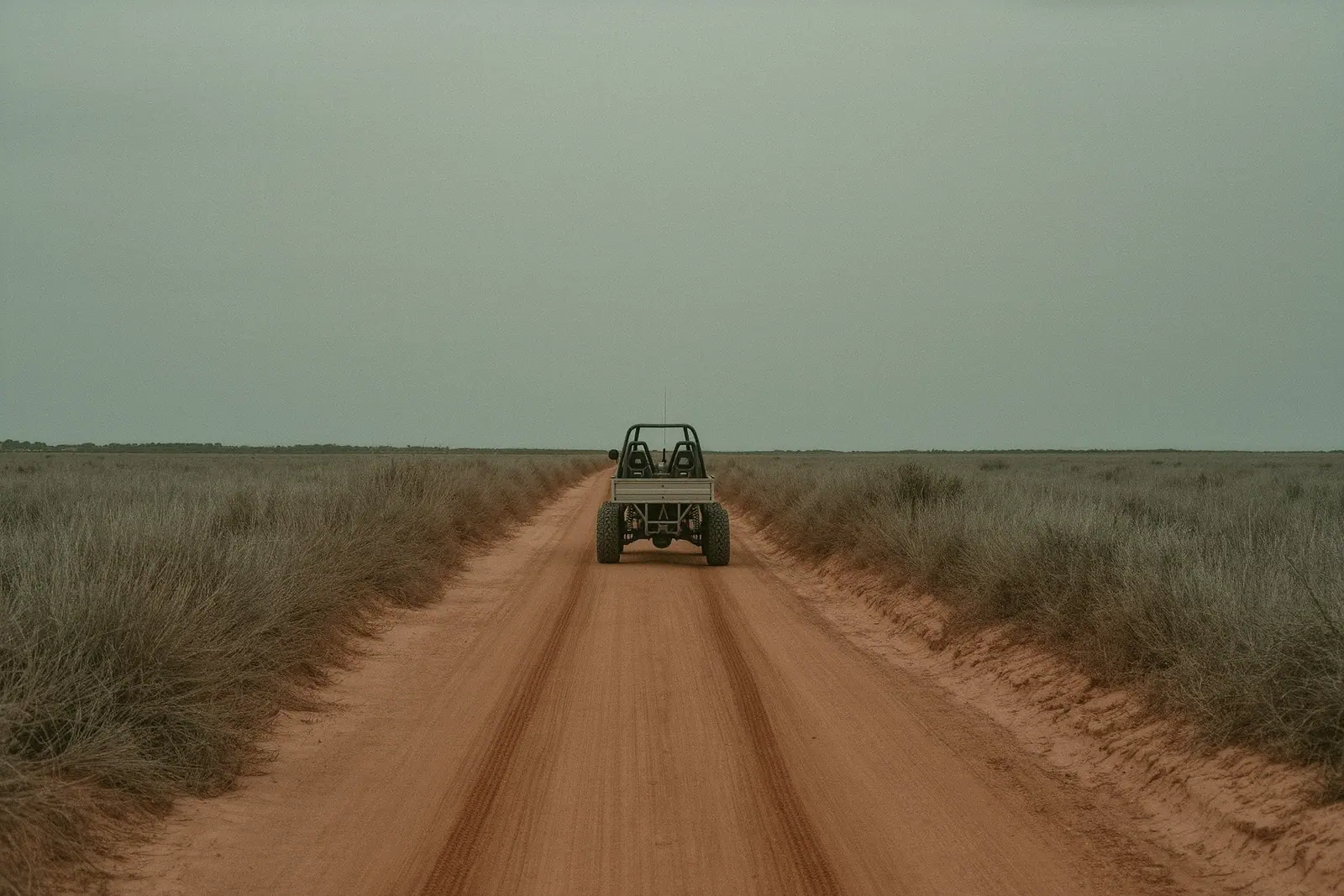 An open-sided buggy parked on a dusty red dirt track in the north of Ibiza, bare roll bar and knobbly tyres, deep wheel ruts in the foreground and dry pine scrub either side.