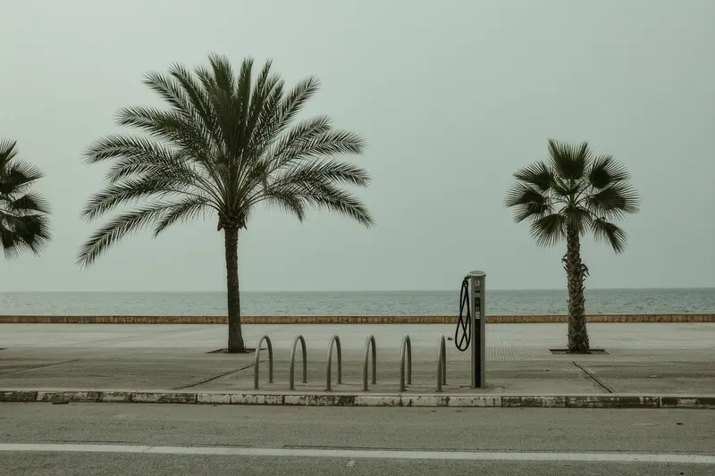 A rental bike stand beside the flat coastal promenade at Santa Eulària, empty racks and a repair post, no riders.